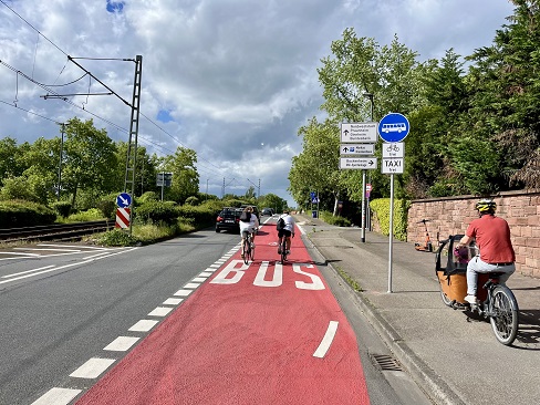 Fahrräder auf einer rot markierten Busspur, auf einem baulichen Radweg rechts fährt ein Lastenrad.