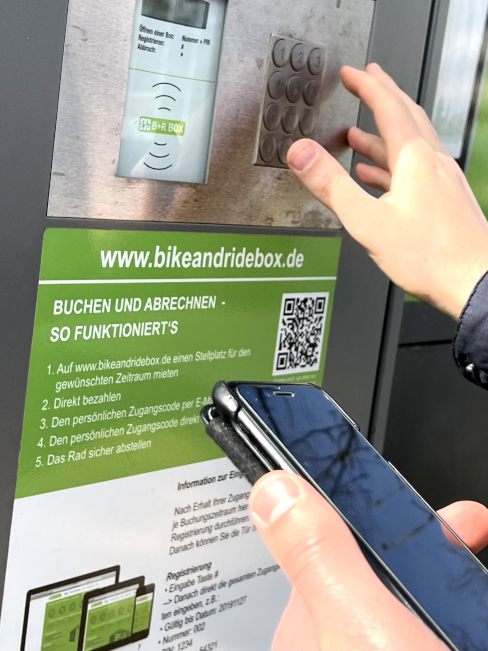 Automat mit Tastenfeld, QR-Code und Smartphone im Bildvordergrund