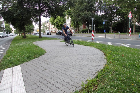 Radfahrender auf dem befestigten Weg eines Mittelstreifens einer Straße mit zwei getrennten Fahrspuren